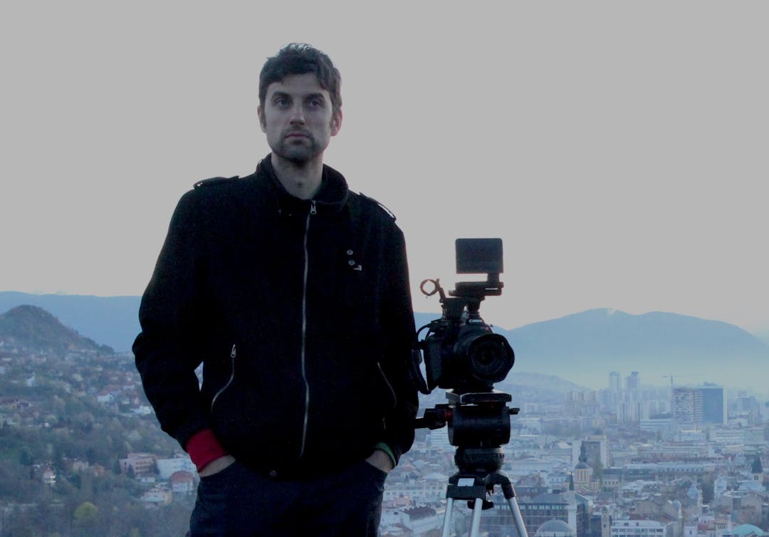 Dusan Solomun standing next to a camera, the city of Sarajevo in the background
